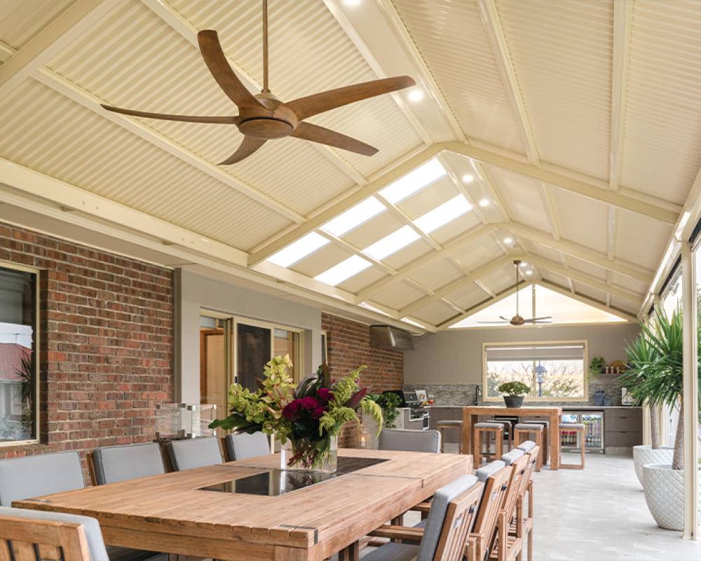 Cream gabled patio with timber furniture and ceiling fans, built with insulated COLORBOND® steel patio roof materials.