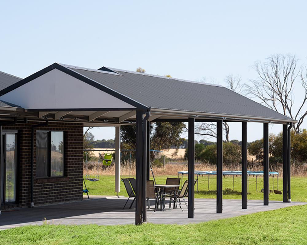Rural home with steel patio roof and black posts, using COLORBOND® steel for durable outdoor patio cover.
