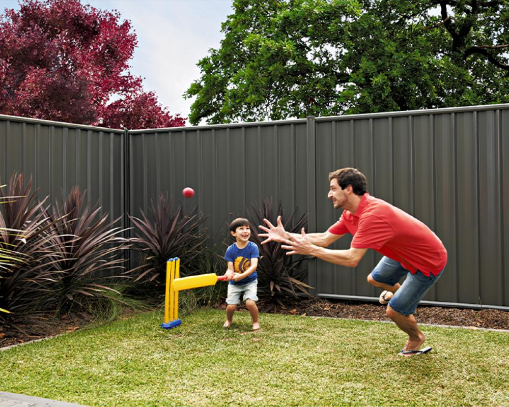 Child playing backyard cricket with steel COLORBOND® steel fencing for low maintenance privacy