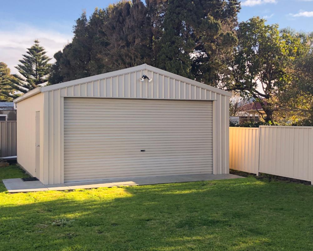 Backyard shed with light COLORBOND steel walls and roller door, showing how Surfmist sits at the lighter end of the colour chart