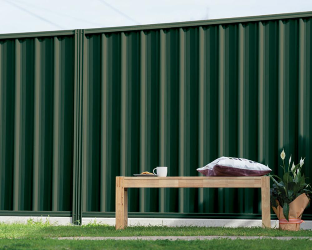 Outdoor seating area beside a dark green COLORBOND steel fence, showing a mid-tone option from the COLORBOND colour chart