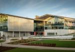 Modern industrial building with a corrugated steel roof, large glass windows, and landscaped surroundings at sunset.